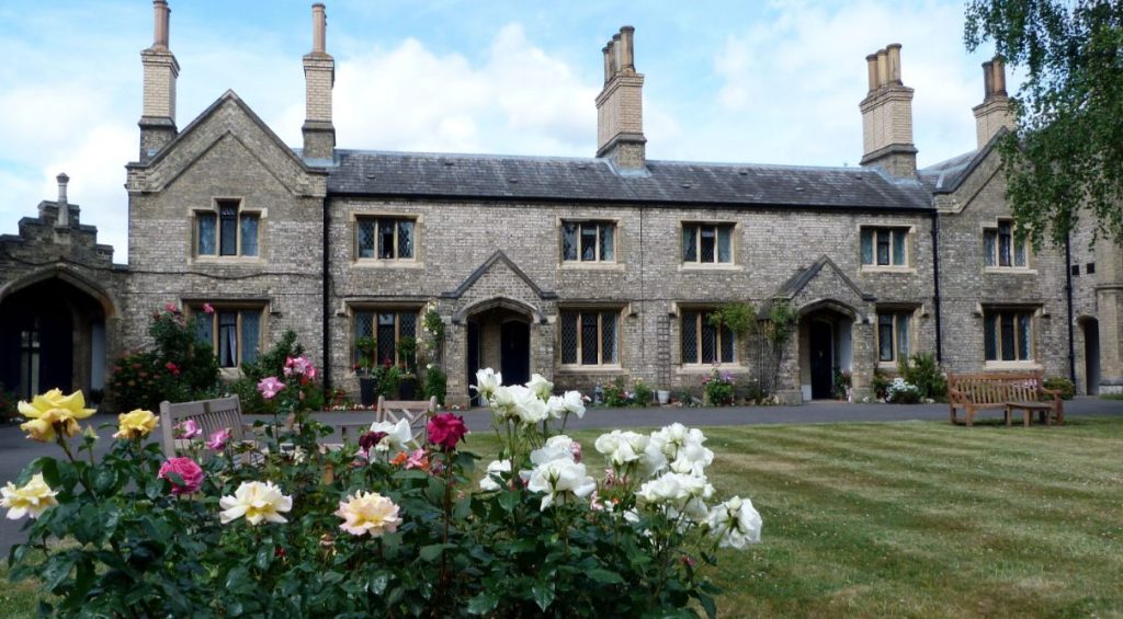 The front of Hickley's Almshouses in Richmond owned by the Richmond Charities, which show a bench, lawn and lots of flowers outside the housing.