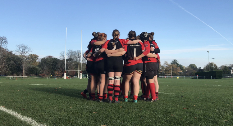 London Welsh Women group huddle before a league game with posts in the background