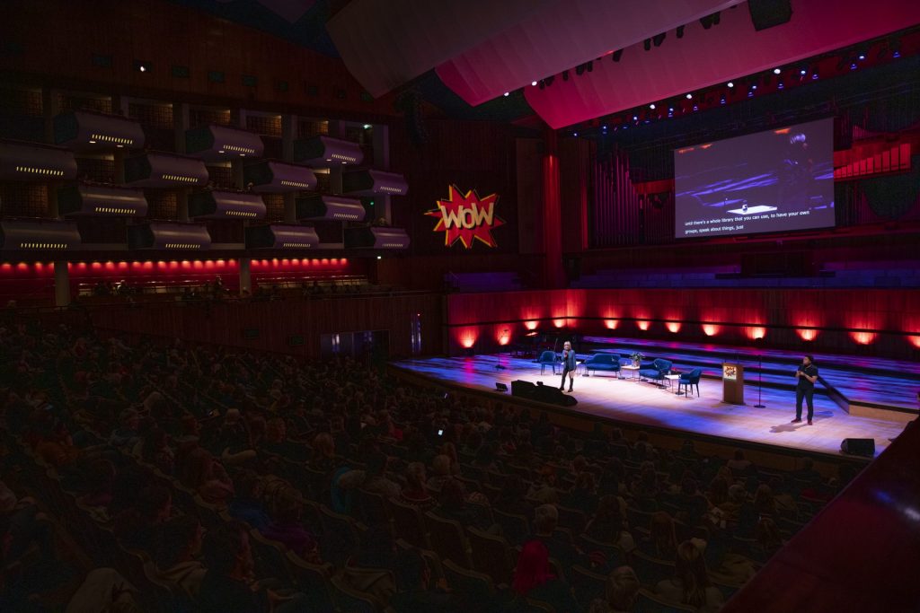 Women in large auditorium listening to Dame Jude Kelly on stage