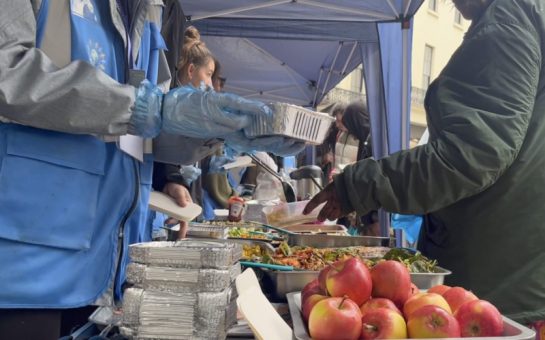 Volunteers from Refuge Network International serve food, including apples and salads, to the homeless and disadvantaged in silver containers