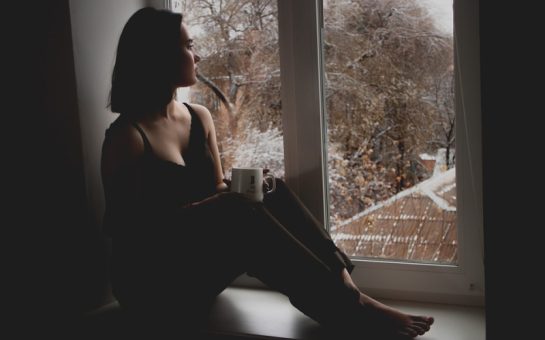 A woman sitting in a dark room looking out a window