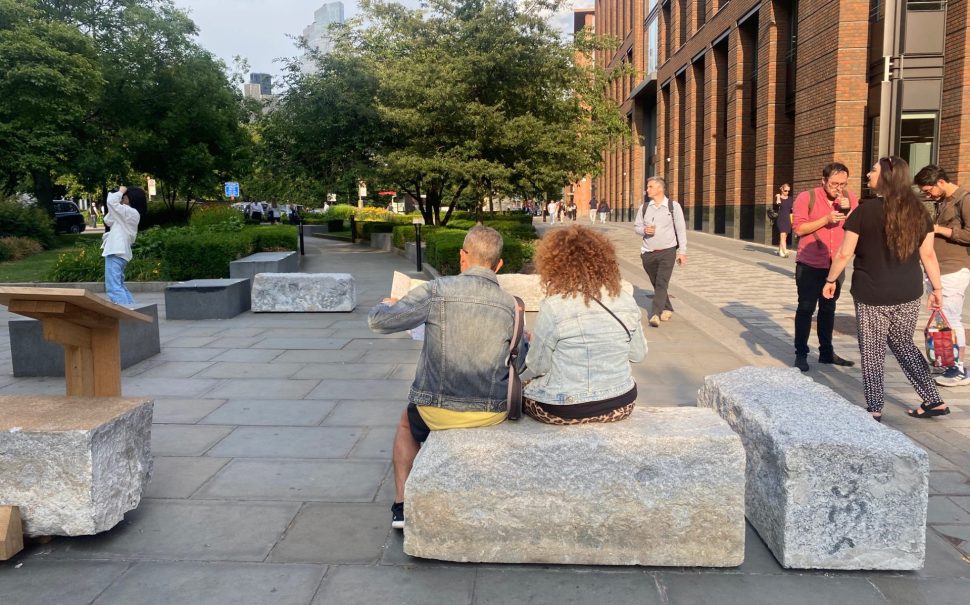 London visitors sitting on a granite stone relocated by the City of London's project "From Thames to Eternity".