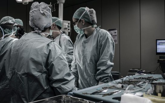 Surgeons in scrubs stand around a surgical table during operation