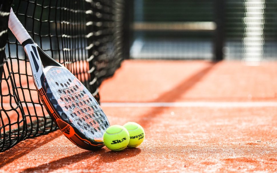 A racket leans against a net with two green tennis balls next to it.