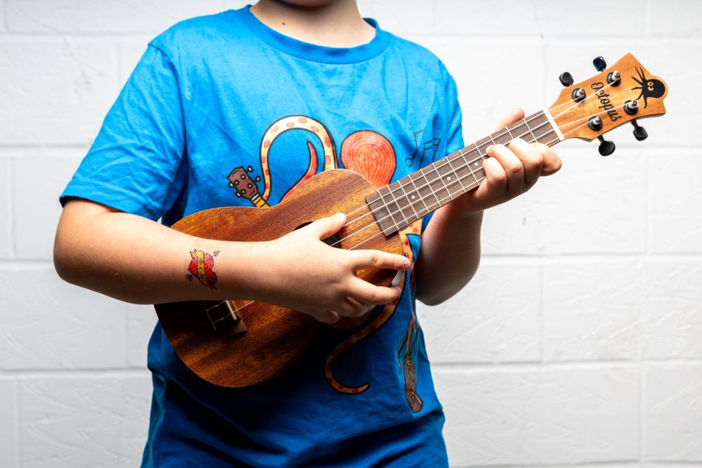 The founder's son with a ukulele the project it donated, wearing a ukulele t-shirt and 'Uke 4 Eva' tattoo.