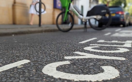 CYCLE in white paint on the road is the main focus. Blurred in the background is a Lime e-bike parked in the cycle parking spot