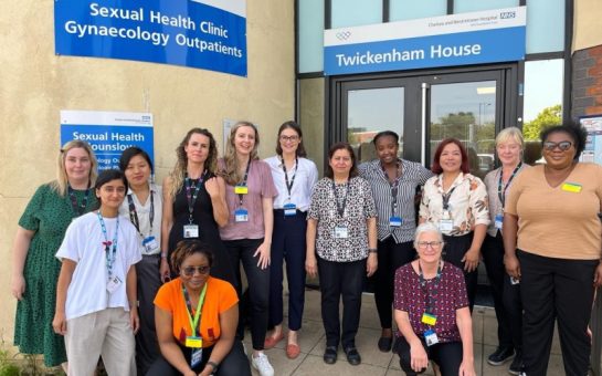 image of 13 members of the sexual health hounslow team. They are standing in front of Twickenham House's Sexual Health Clinic for gynaecology out patients.