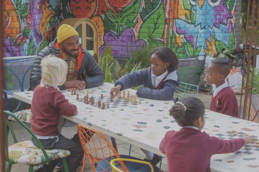 Children from Chesterton Primary School in Battersea try out some chess moves with the help of teacher Edress Kheir on the specially designed table and Jay Blades designed chairs from the London Square Community Garden, now a centrepiece in the roof garden on the Doddington estate in Battersea