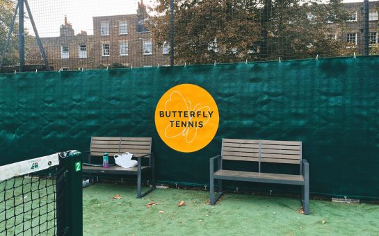 Glorious mustard Butterfly Tennis Club sign between two benches on a green tennis court