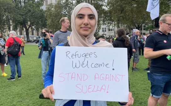 Protestor stands with placard Reading ‘Refugees Welcome! Stand Against Suella!”