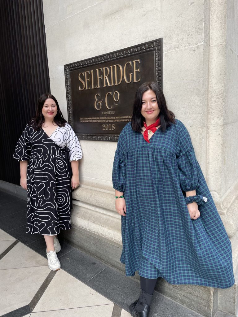 Liv and Daisy pose in front of a Selfridges & Co plaque outside the shopfront.  