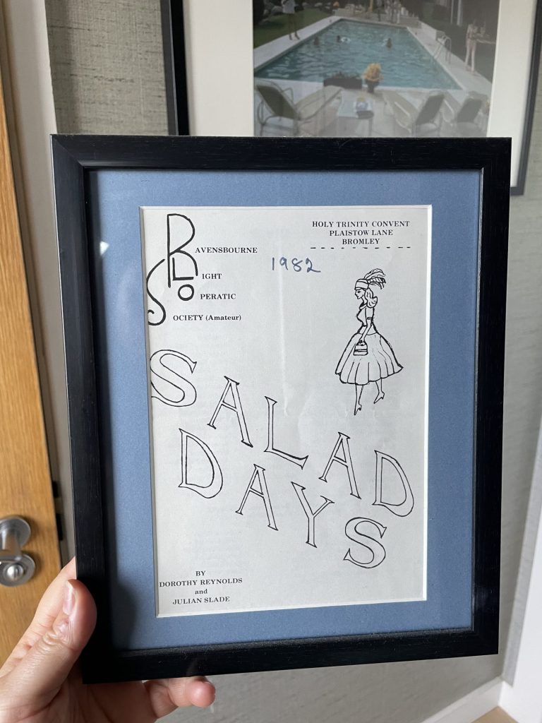 Liv holds up a framed vintage theatre booklet from Beryl's collection for a production of Salad Days. 