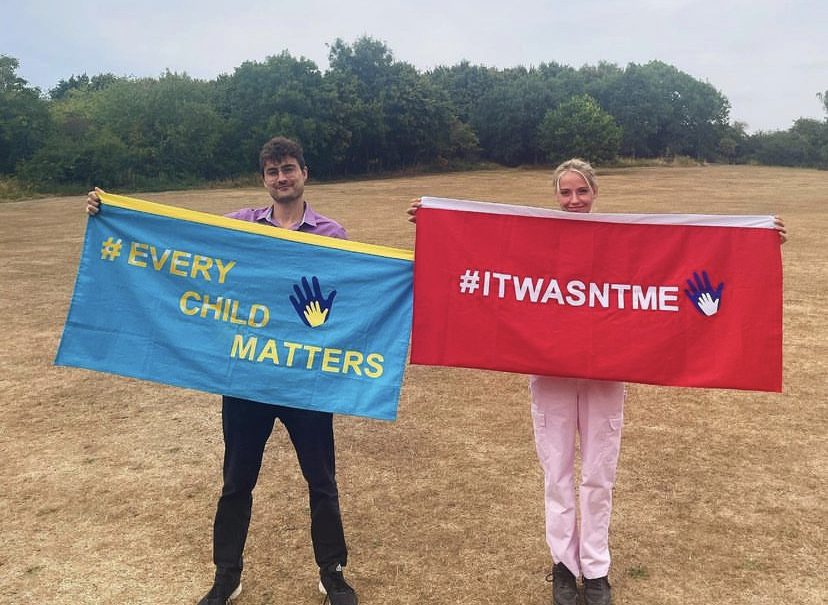 After the announcement of Jade's Law, two child victims of parental imprisonment are holding flags. One is blue with the words 'Every child matters'. The other is a red flag with the words 'It Wasn't Me'.