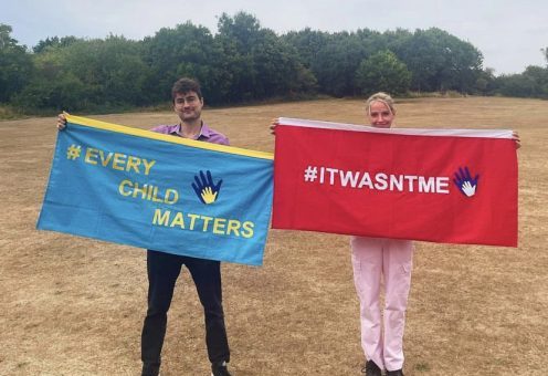 After the announcement of Jade's Law, two child victims of parental imprisonment are holding flags. One is blue with the words 'Every child matters'. The other is a red flag with the words 'It Wasn't Me'.