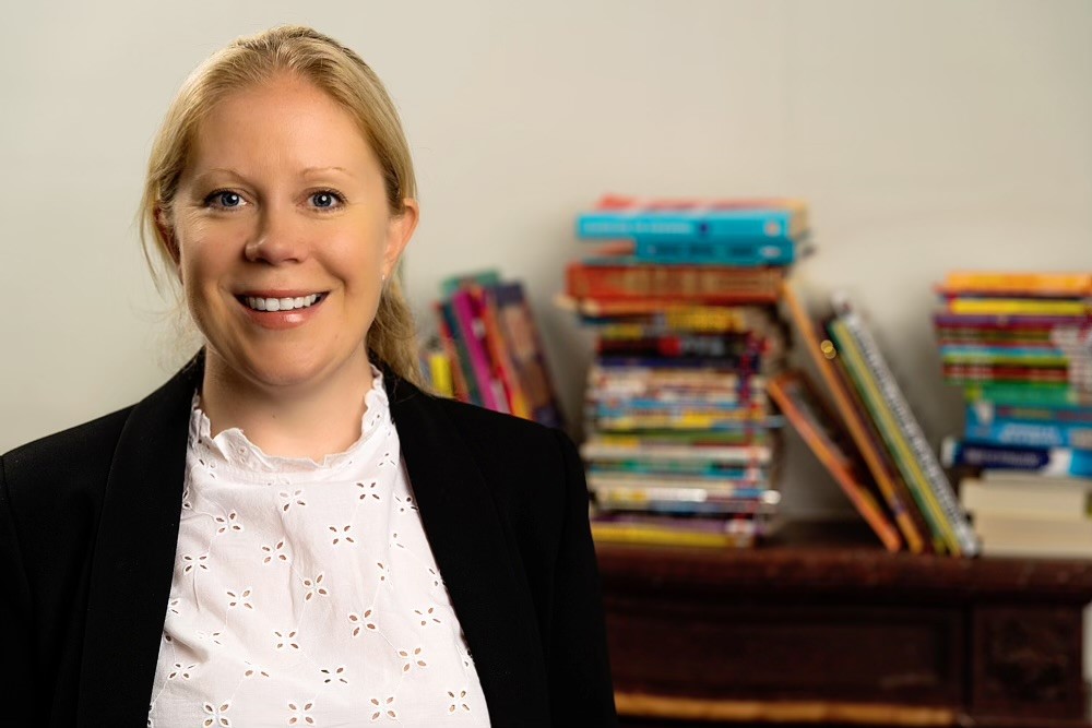A headshot of Doorstep Library's CEO, Katie Bareham, with piles of books stacked in the background.