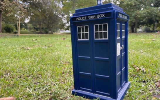 A blue Tardis toy placed on grass with trees in the background, in the same spot the Tardis landed in Kingston 50 years ago