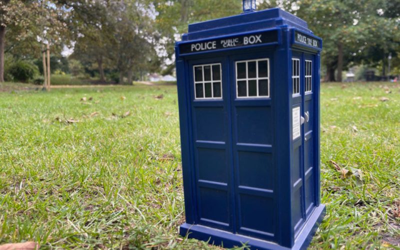 A blue Tardis toy placed on grass with trees in the background, in the same spot the Tardis landed in Kingston 50 years ago