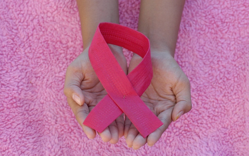 Hands holding a breast cancer pink ribbon against a pink background