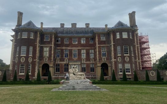 a picture of Ham House on a cloudy day. In front of the manor is a grey statue of "Father Thames" as a river god reclining on a stone plinth.