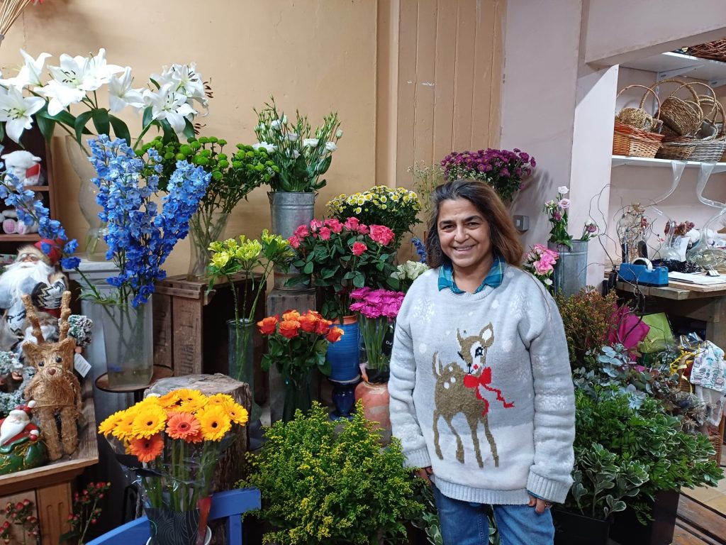 Jamila, a woman, standing in front of a floral display in her shop. 
