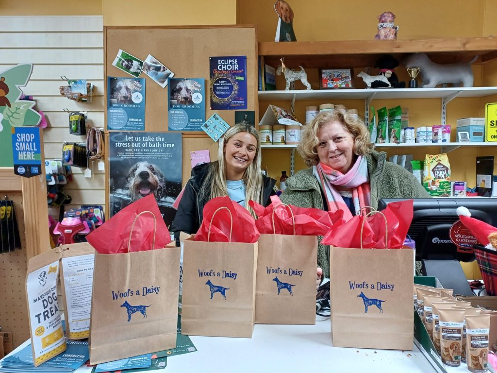 Two women stand behind a till with goody bags in front of them