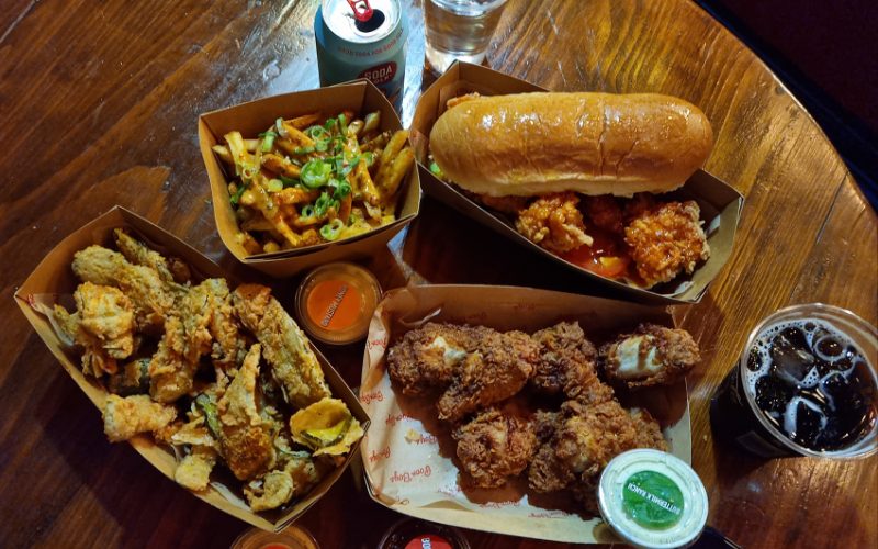 A wooden table full of Shrimp Po, Fried Pickles, Chicken Wings, Cajun Fries and drinks.