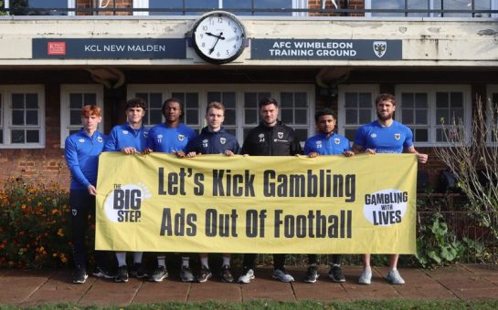 AFC Wimbledon holding up a sign produced by the Big Step campaign which reads: "Let's Kick Gambling Ads Out Of Football"