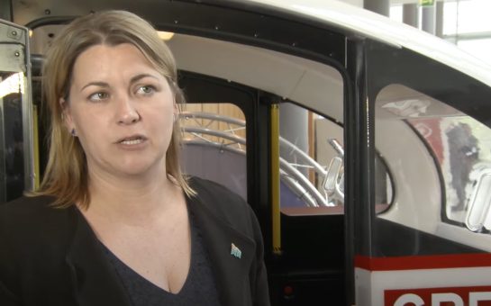 An image of Baroness Liz Sugg, standing in front an autonomous vehicle.