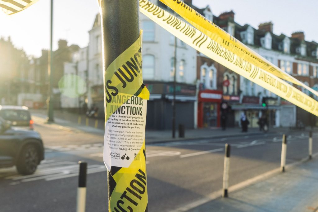 A flyer featuring information on London Cycling Campaign is posted on a lamppost marked with crime scene tape marked 'Dangerous Junctions'