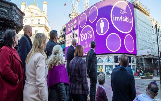 Pedestrians view Piccadilly Lights as it turns purple.