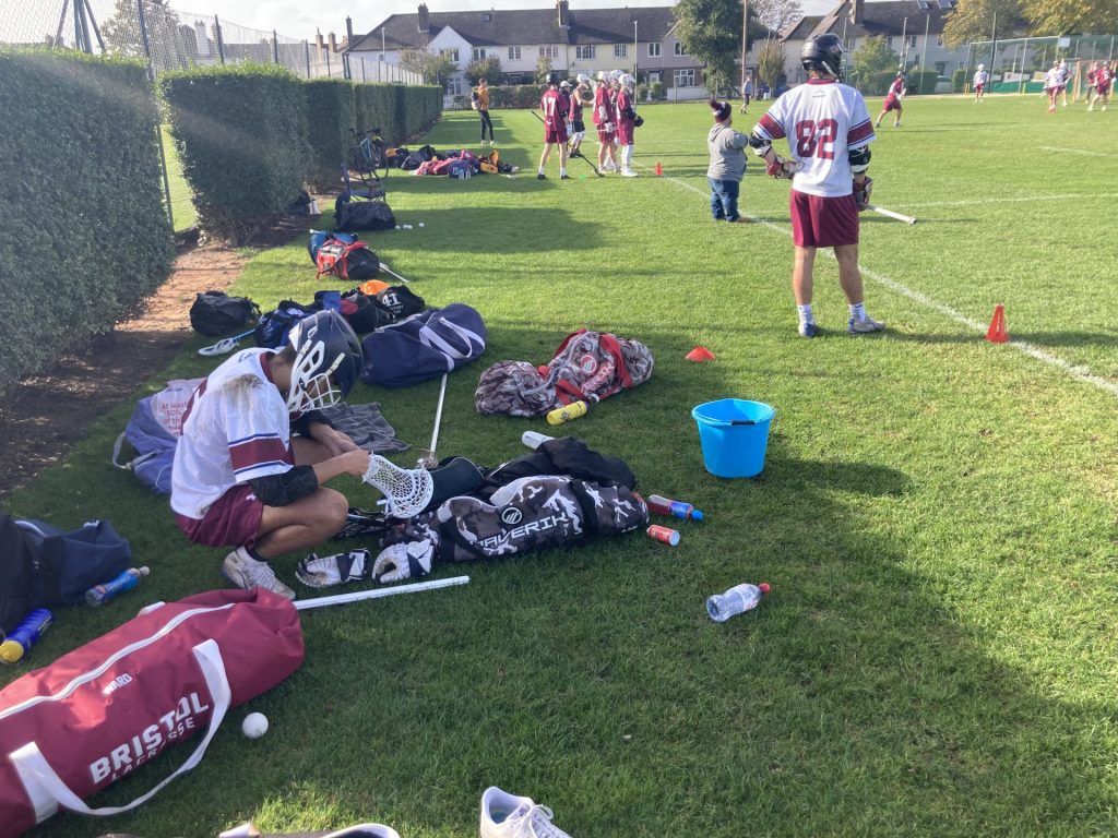Kit, helmets and stick players use during a game of lacrosse, with this player fixing his after a collision.