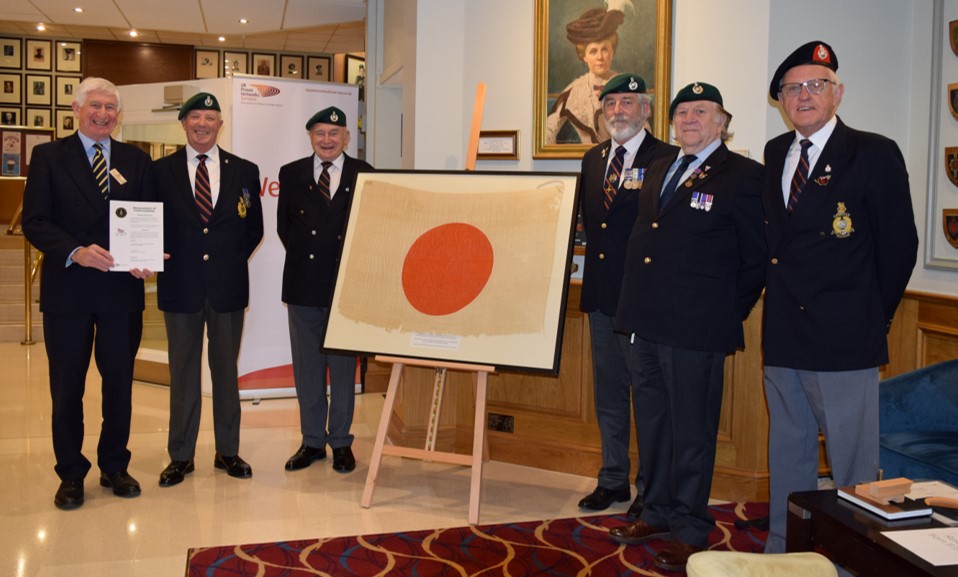 Hugh Player accompanied by other Veterans standing in front of a Japanese surrender flag which a Royal Marine Lieutenant received in Penang, Malaysia, 1945.