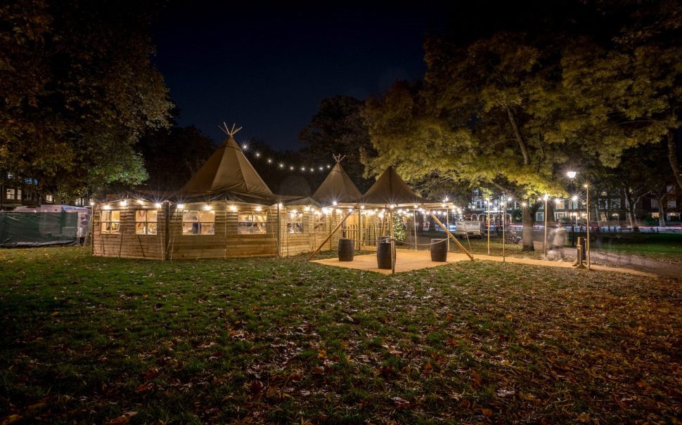 Wooden tipis on Parsons Green with lights decorating the tipis.