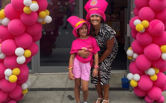A mother and her daughter in front of a balloon arch with pink hats on for brain tumour research