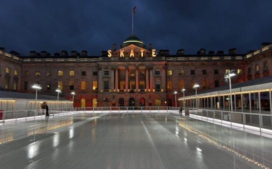 Picture at night has Somerset House in the background with the lit up lights in gold spelling out skate. Foreground is an ice rink.