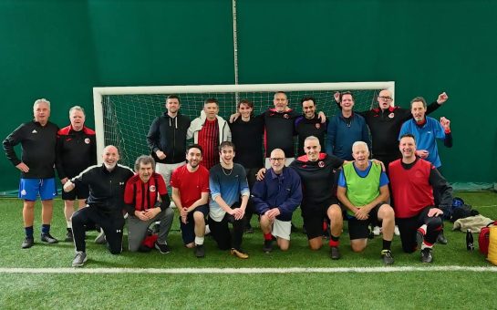 The Parkinson's Fighting Fit Football Team, consisting of eighteen men, smile at the camera as they have their photo taken.