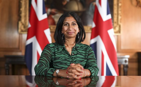 Suella Braverman sat at a table in front of two Union Jack flags