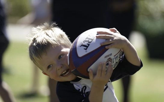 young child running with rugby ball smiling