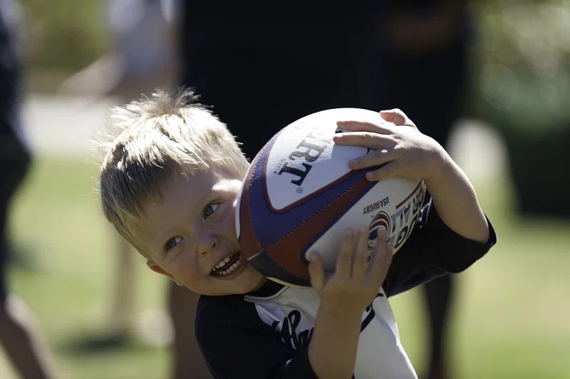 young child running with rugby ball smiling