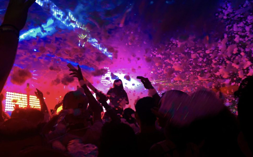 Inside a nightclub with purple and blue flights, sillouetes of clubbers with their hands up are at the bottom of the image. Confetti falls from the ceiling. Used to represent Kingston Pryzm in London.