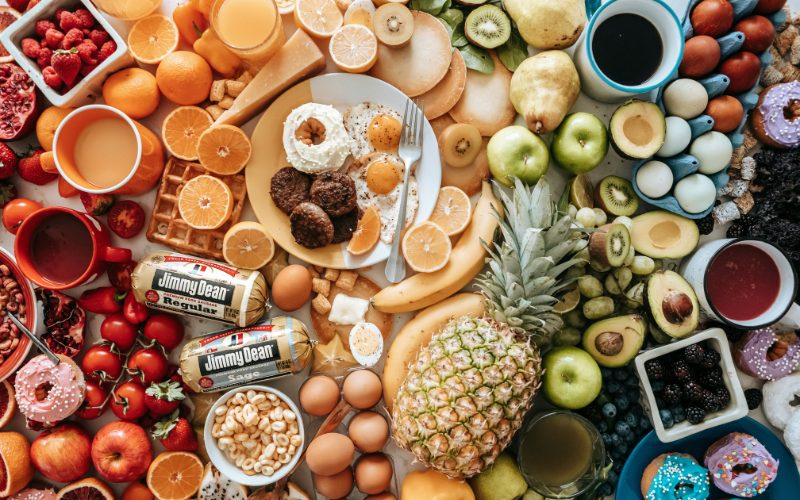 A colourful array of different foods. There is everything from a whole pineapple to donuts and pancakes.