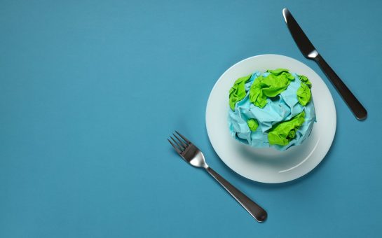 Image of paper globe on a plate with a knife and fork on blue background