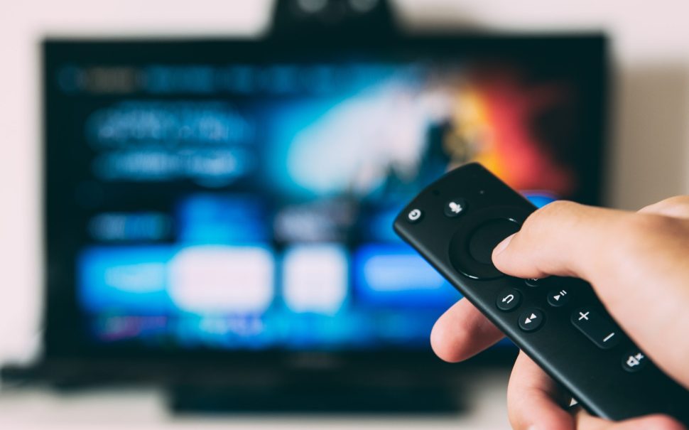 Hand holding TV remote directed at television set