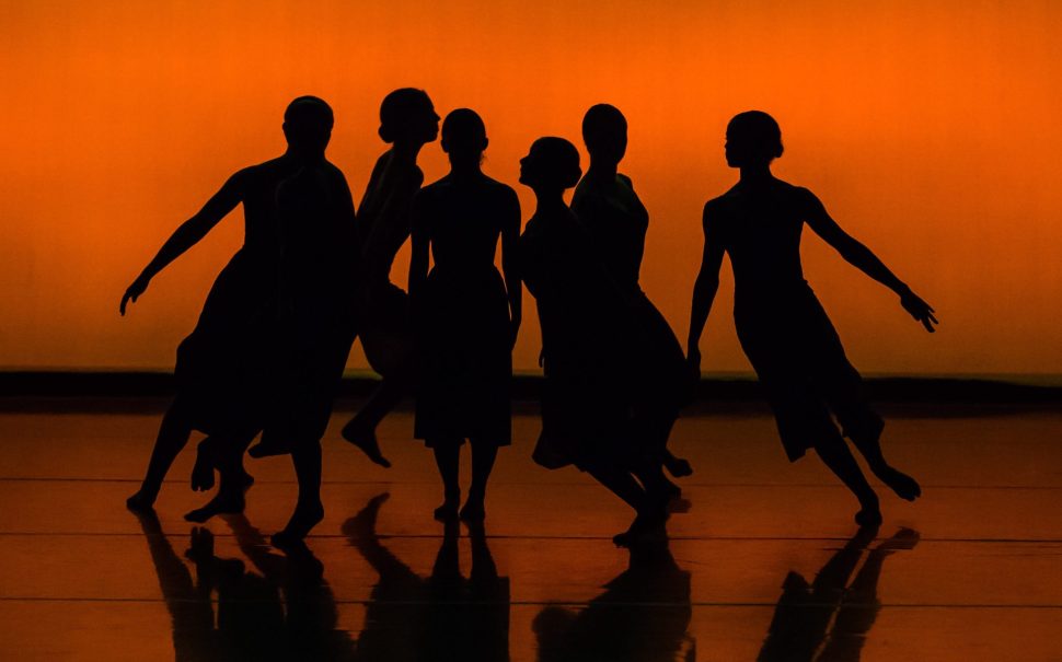 black outlines of dancers with an orange background on a stage.