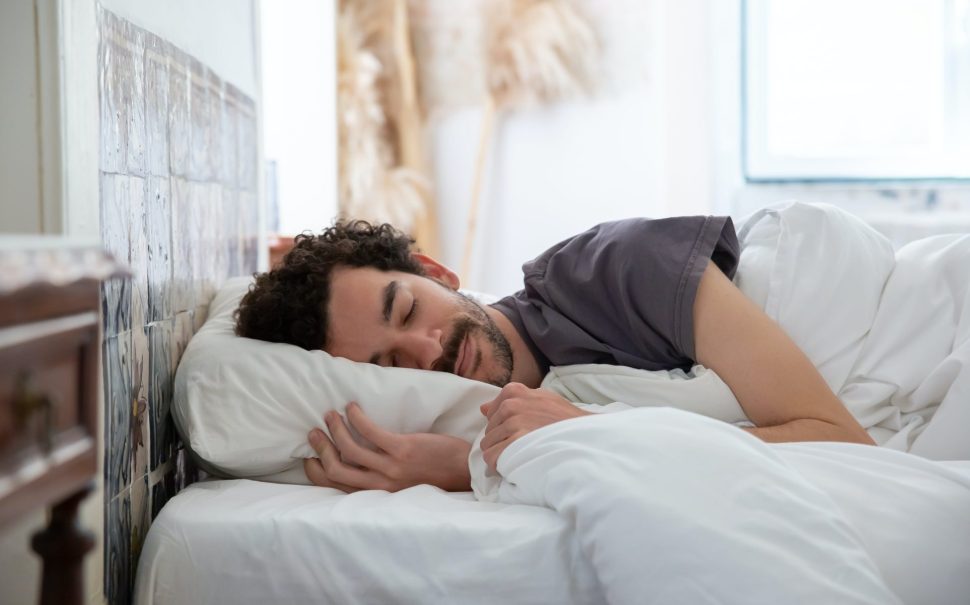 Man with black hair sleeping in bed with white bed sheets