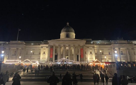 picture of the christmas market at Trafalgar Square. There are tents and fairy lights strung up in front of the National Gallery