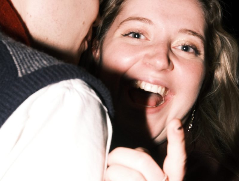 Woman looking joyful at camera smiling whilst man snuggles into her neck.