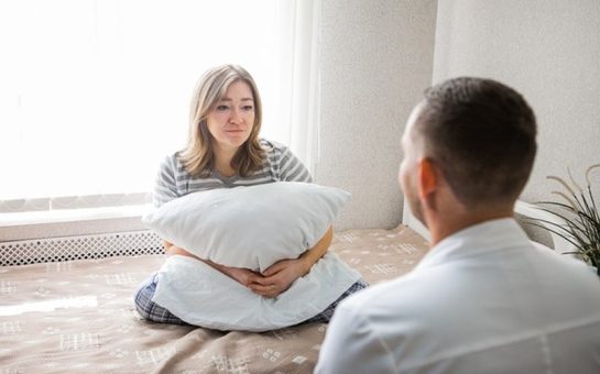 A woman, possibly suffering from mental health disorders, sits on a bed to receive some councilling