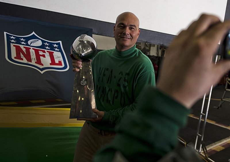 Master Chief Aviation Electronics Technician Robby Bonanno poses for a photo with the Vince Lombardi trophy in the hangar bay of the Nimitz-class aircraft carrier USS Carl Vinson