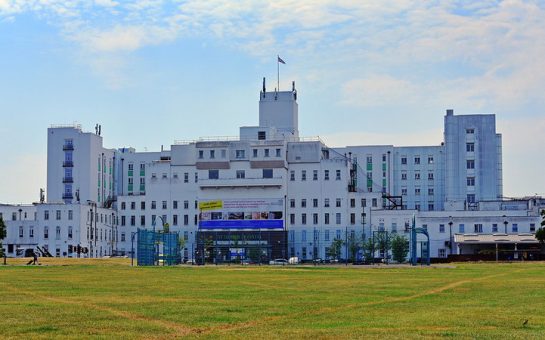 Wide view of white hospital buildings showing grass below and sky above.